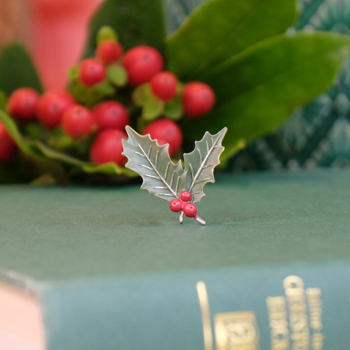 Alexander Thurlow Holly Christmas Brooch on a book with flowers in the background ATH723